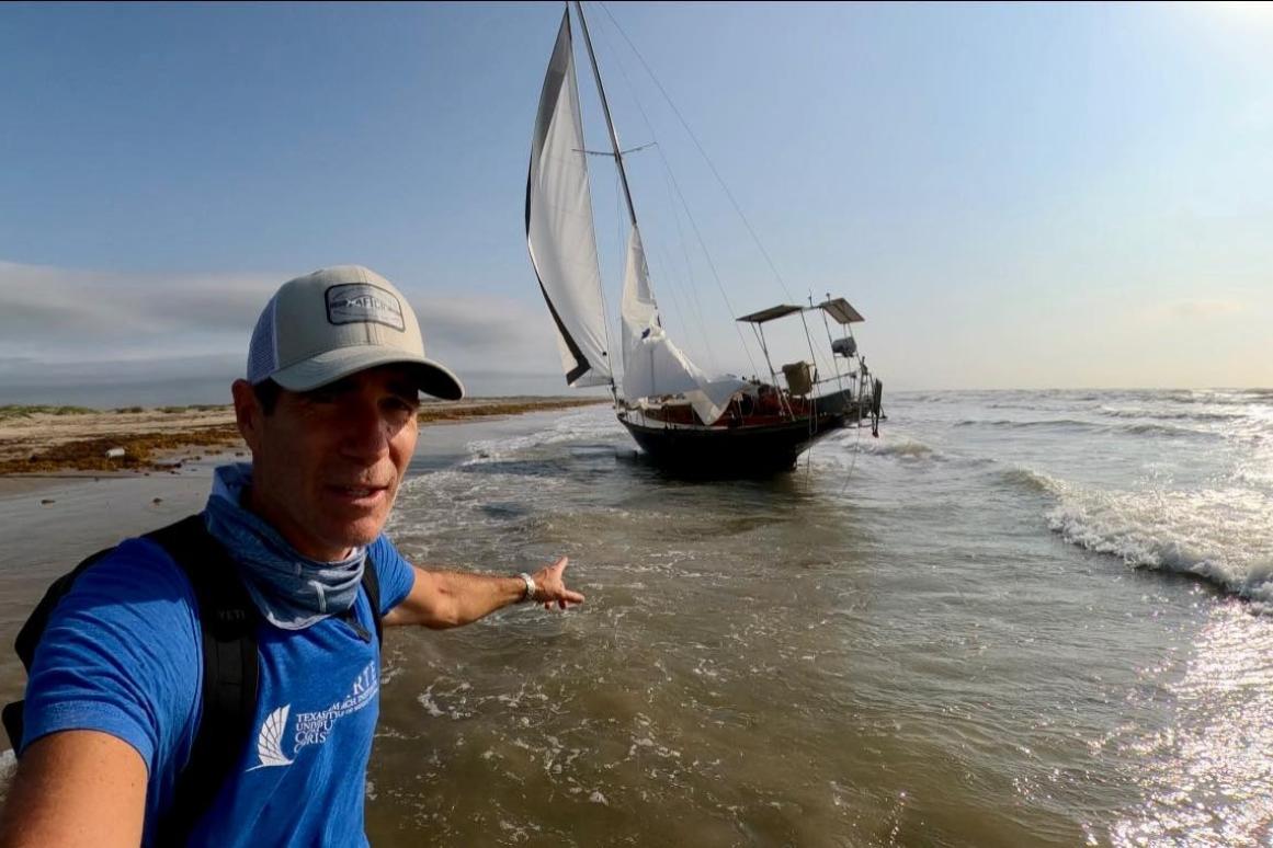 HRI Director of Community Engagement Jace Tunnell points to an abandoned sail boat on a beach. 